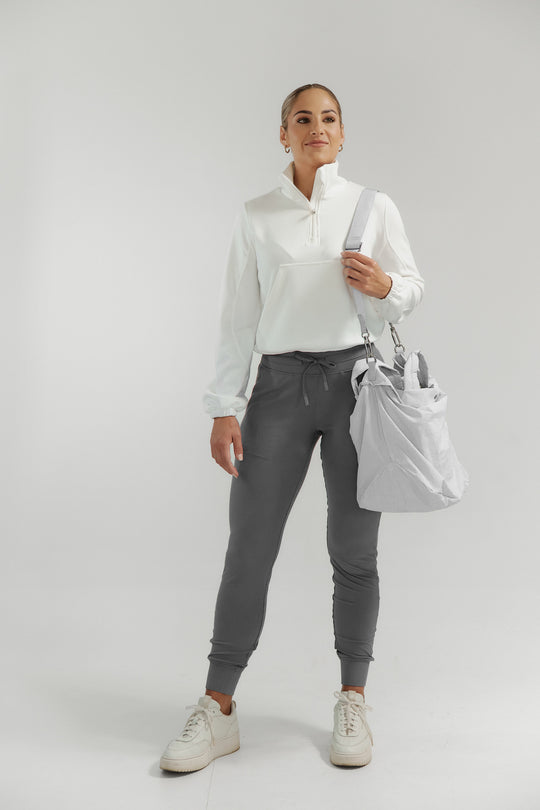Woman wearing a white shirt, gray pants, and white sneakers on a plain background