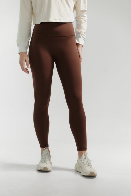 Person wearing brown leggings and white sneakers on a light gray background