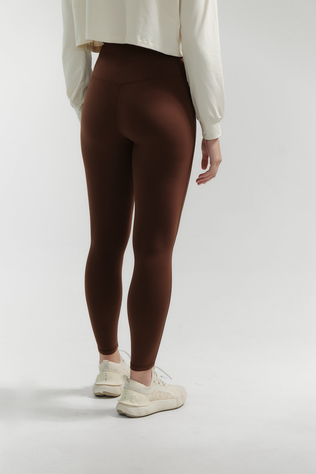 Person wearing brown leggings and white sneakers on a plain background