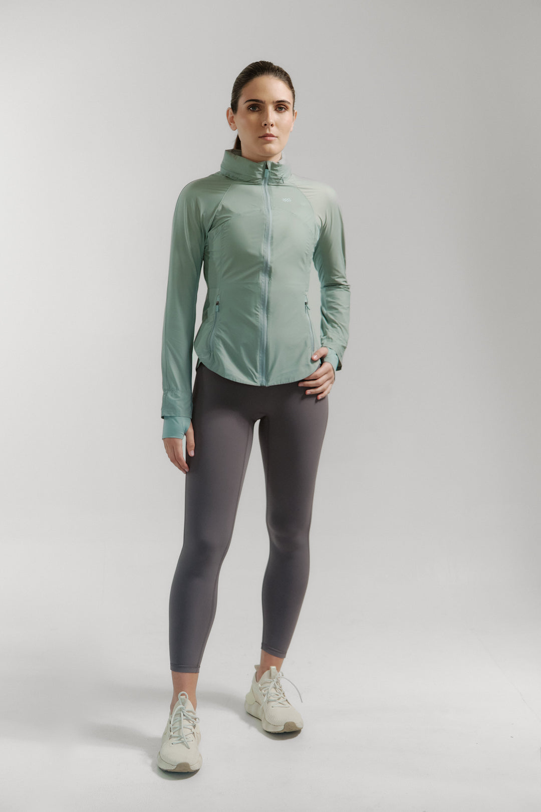 Woman wearing a green jacket and gray leggings on a white background
