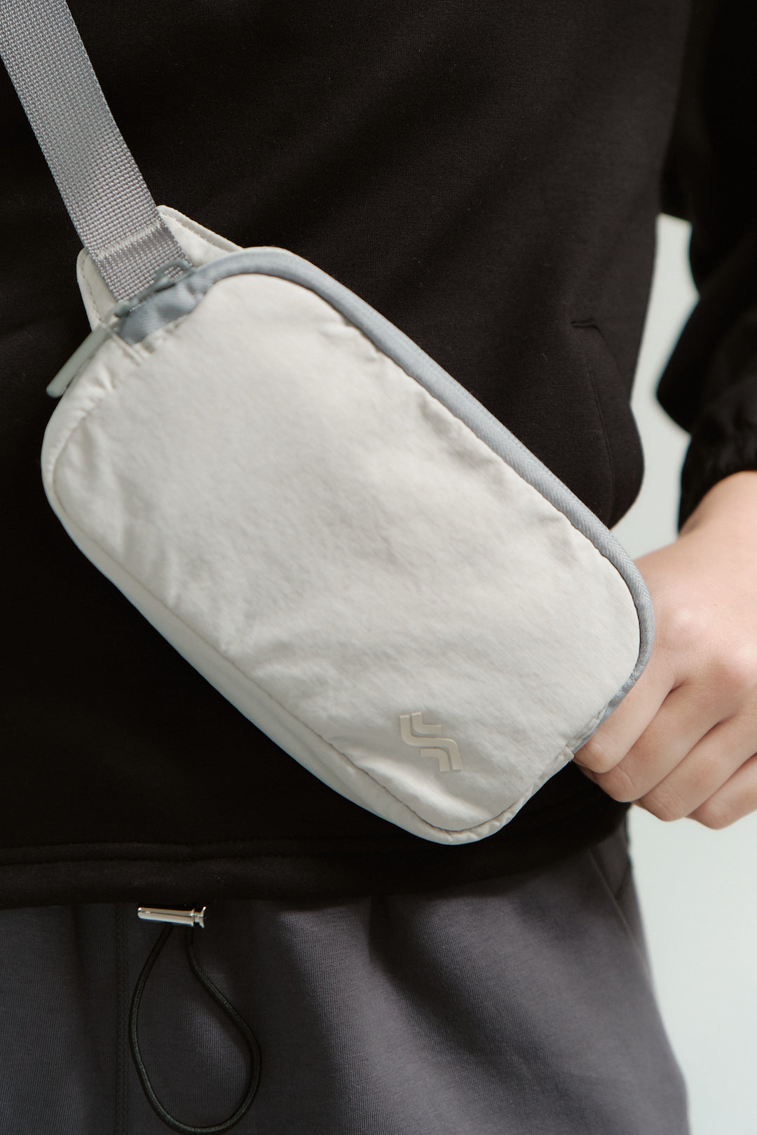 Person holding a gray waist bag with a visible brand logo.