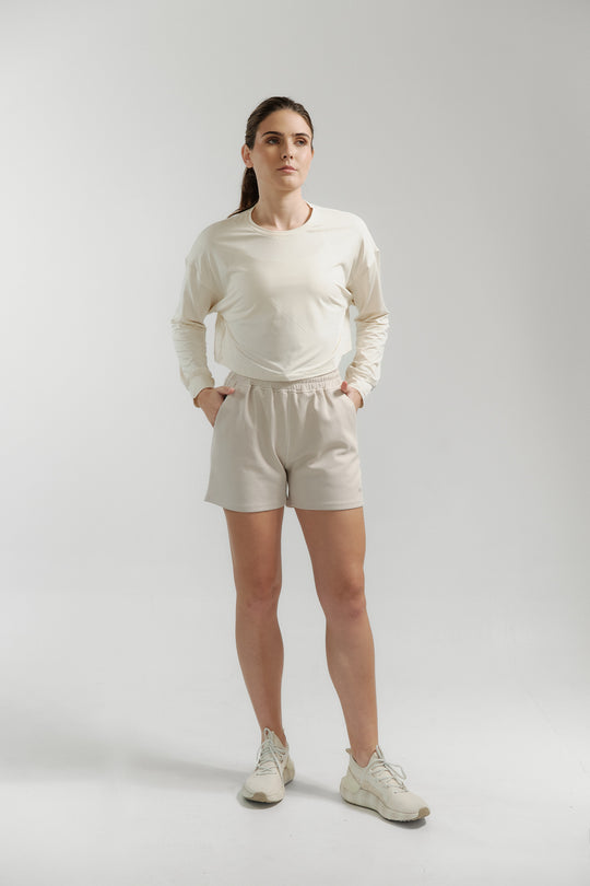 Woman wearing a white long-sleeve shirt and beige shorts on a light gray background