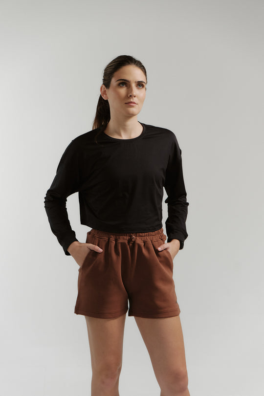 Woman wearing a black long-sleeve shirt and brown shorts on a white background