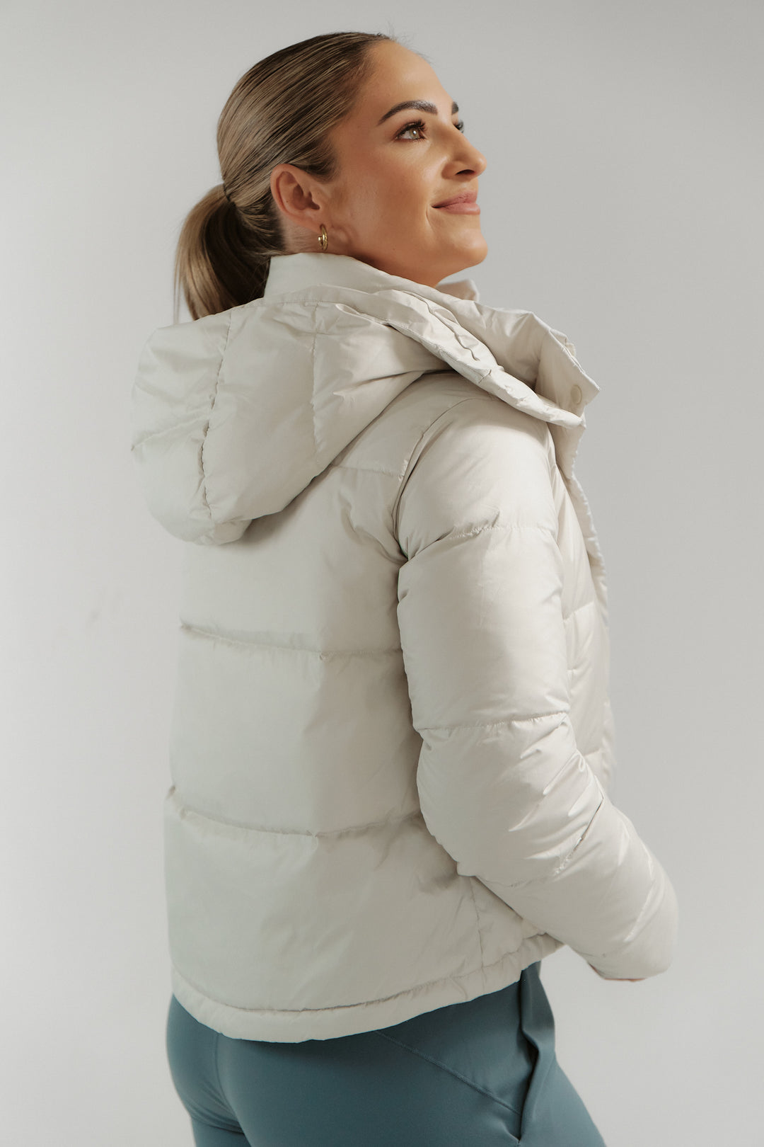 Woman wearing a light gray puffer jacket against a plain background